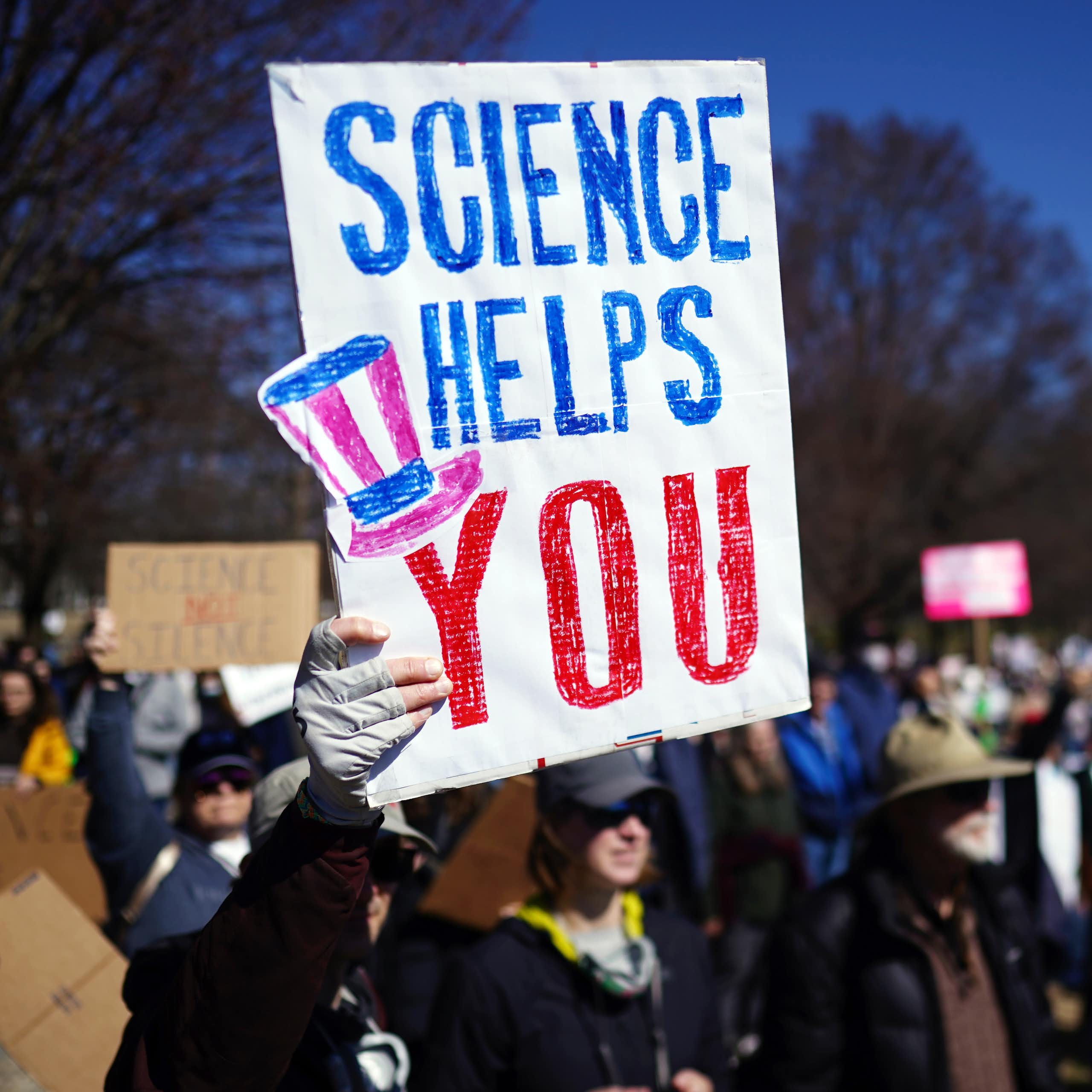 A sign saying science helps you held up by a protestor. 