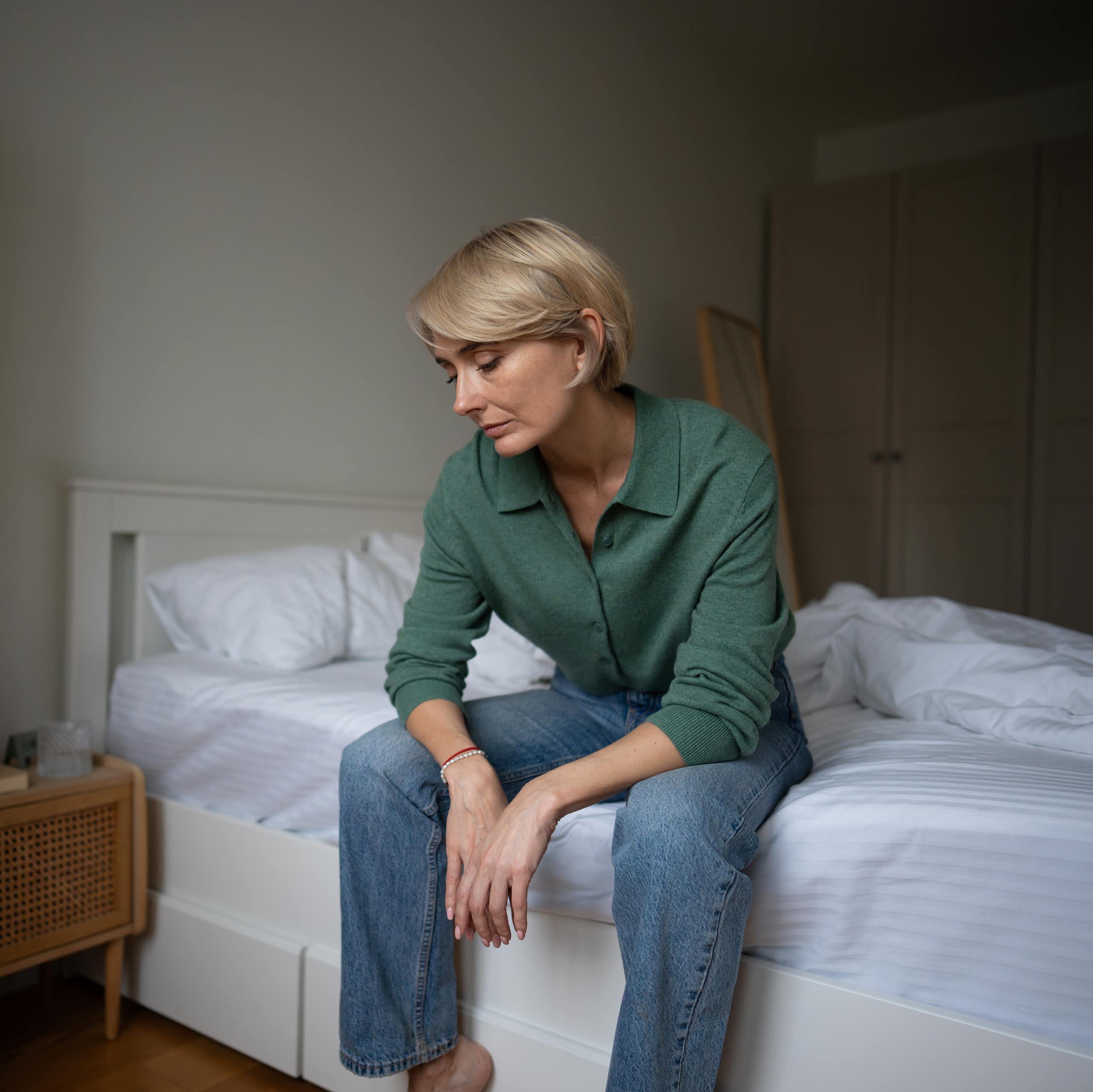 Tired looking woman sitting on the edge of a bed.