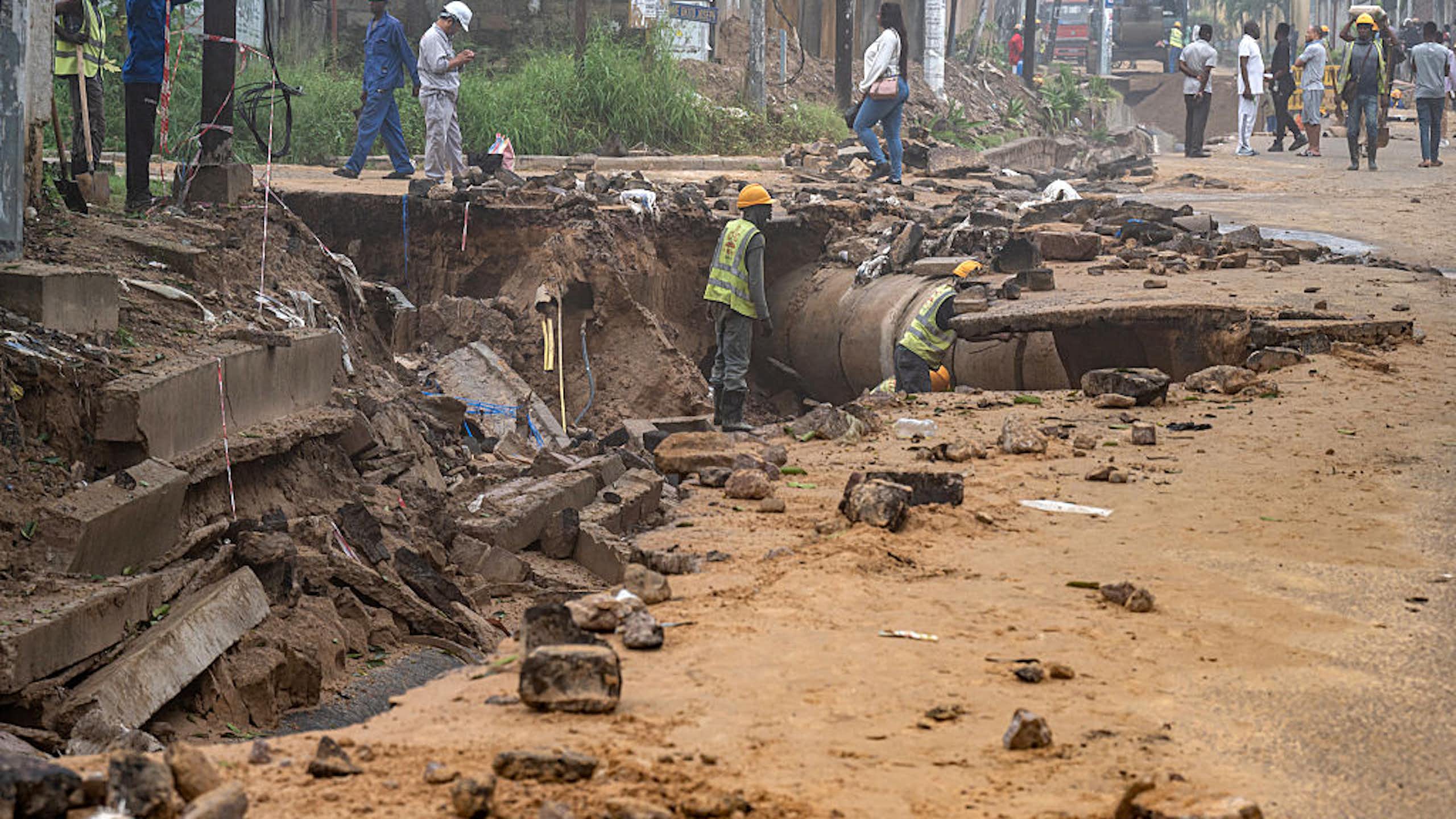 Workers in hard hats looking at a road that has been damaged