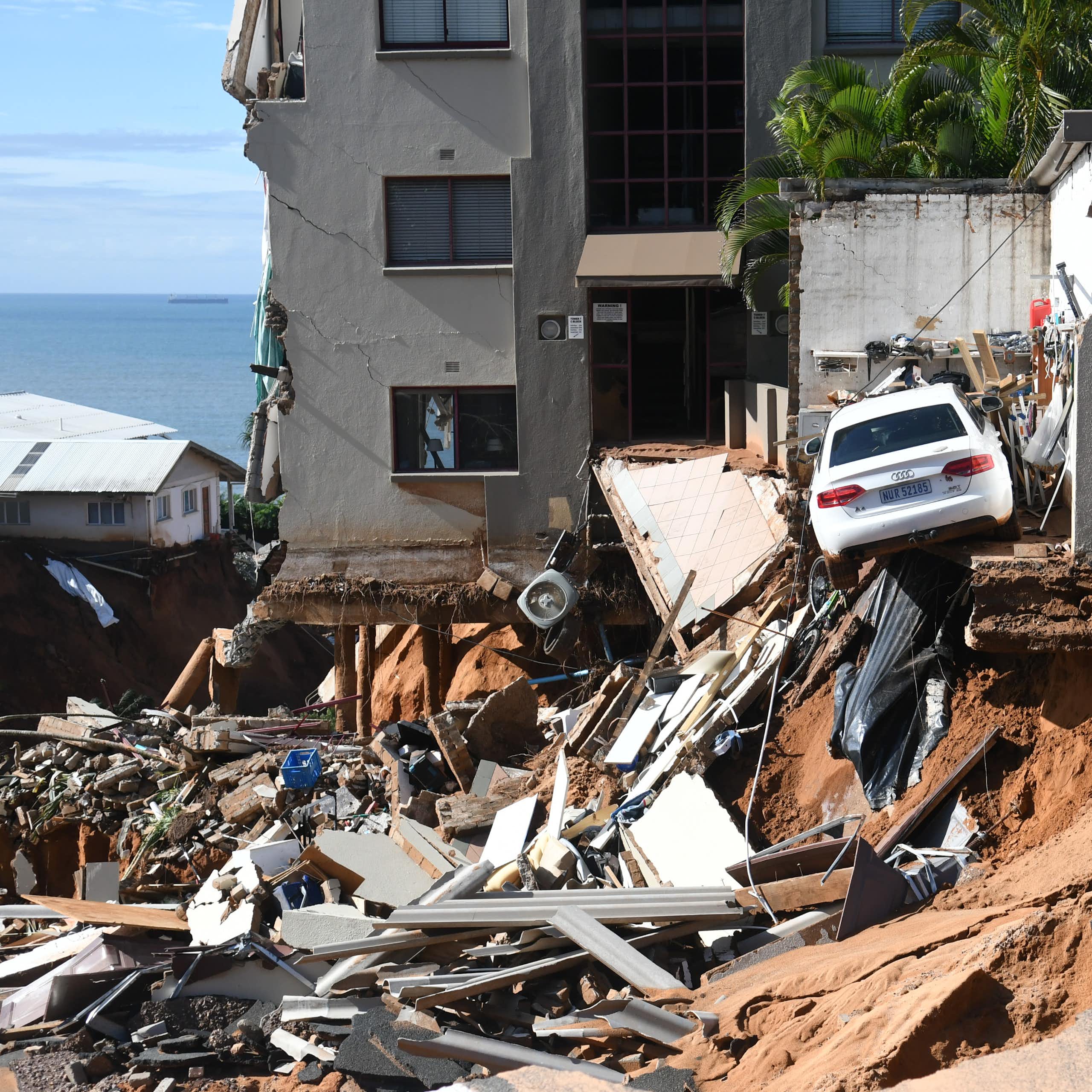 An urban four-storey building where the bottom storey and a parking lot have been washed away by floods