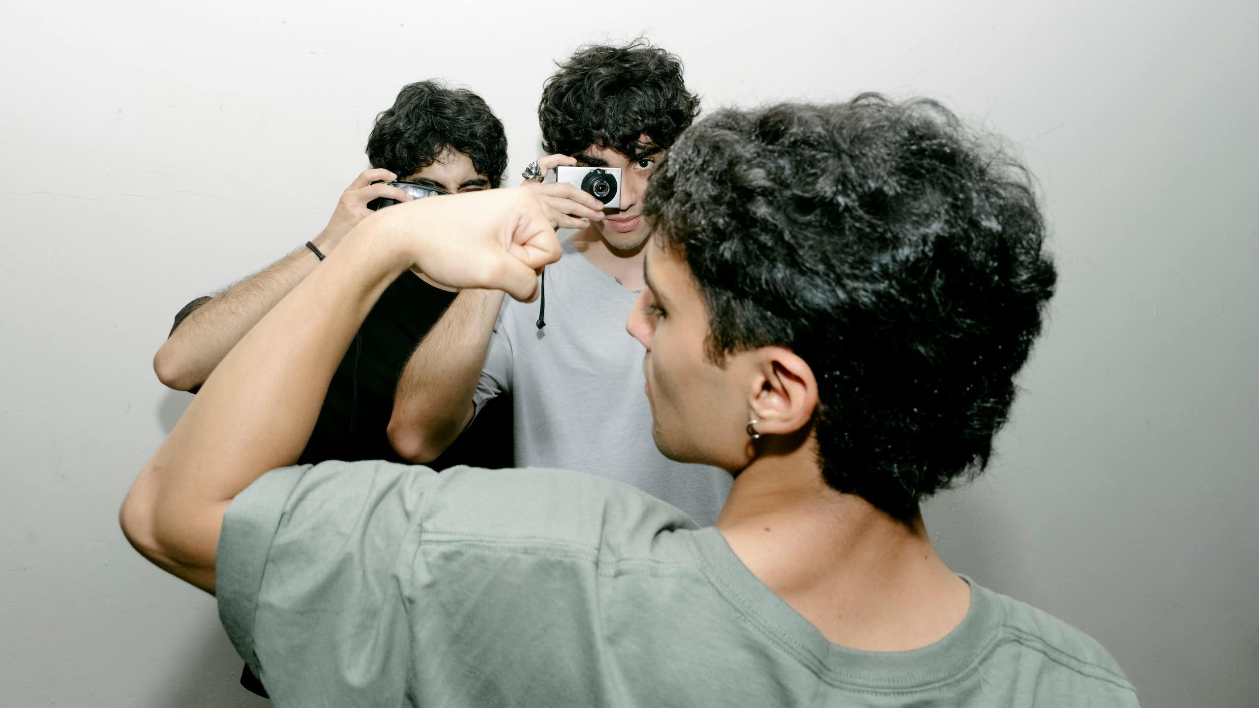A young man flexing while two others are taking photographs of him.