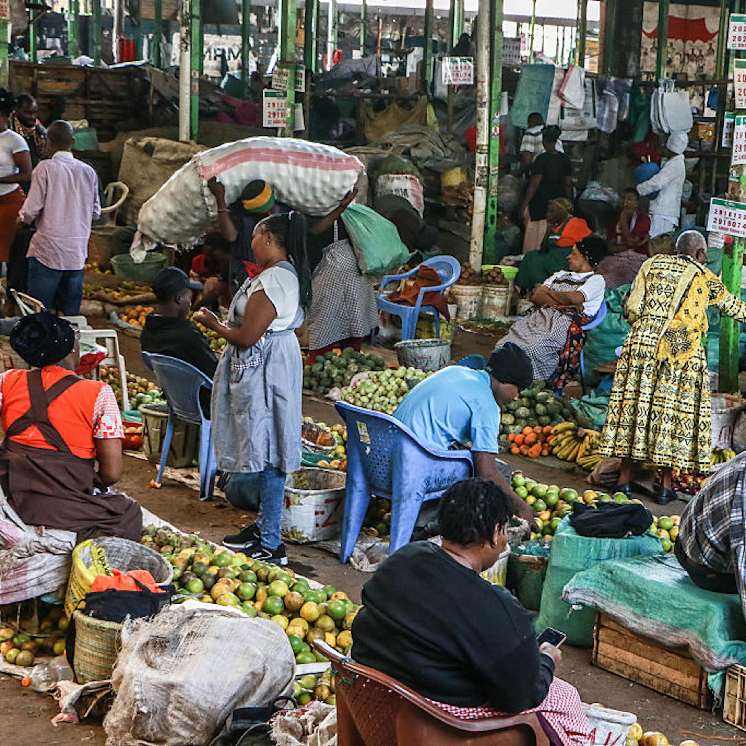 Women seated behind piles of fresh produce on the ground in a marketplace