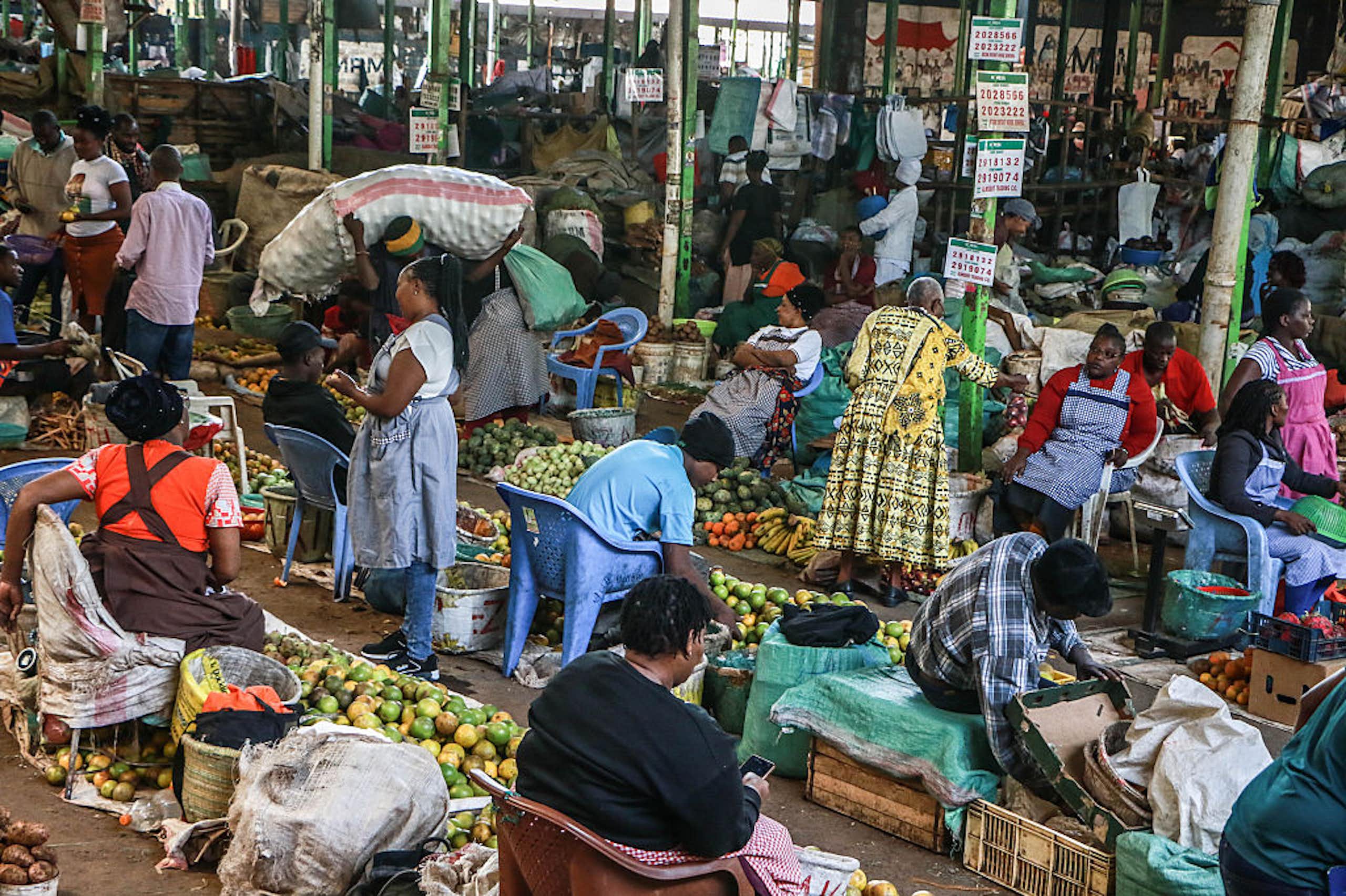 Women seated behind piles of fresh produce on the ground in a marketplace