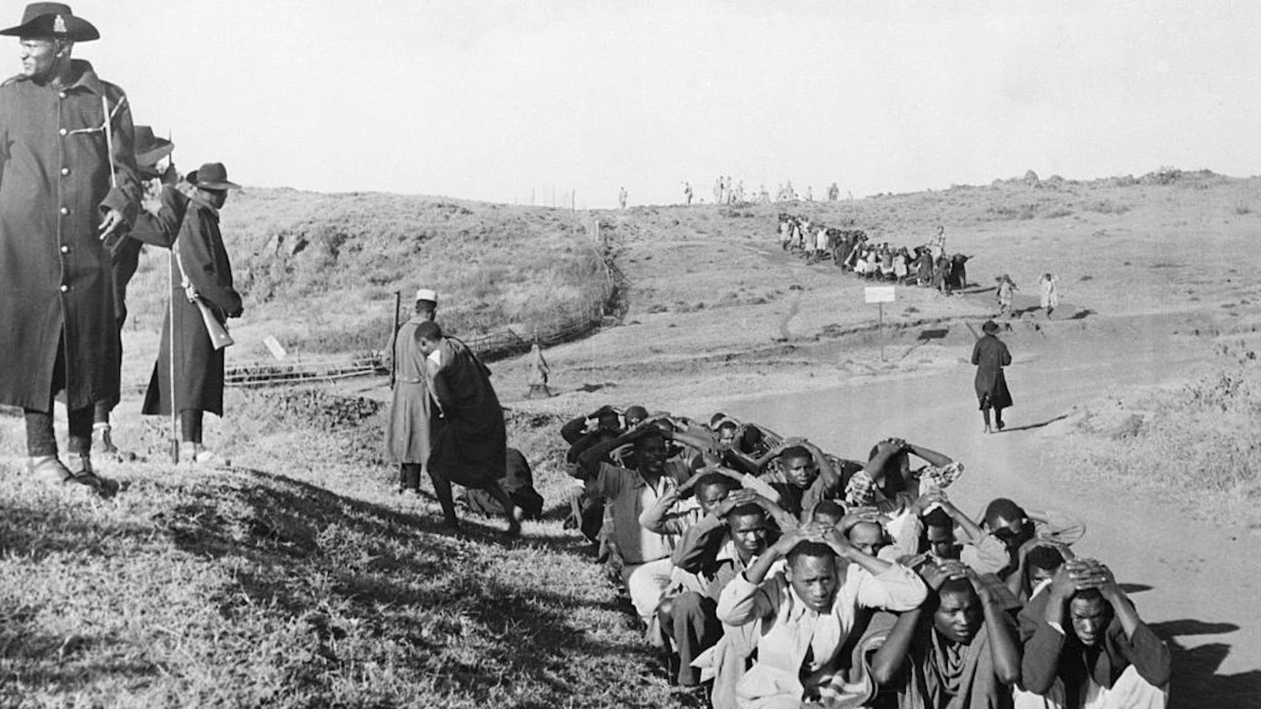 Men huddled on the ground while two others stand towering over them.