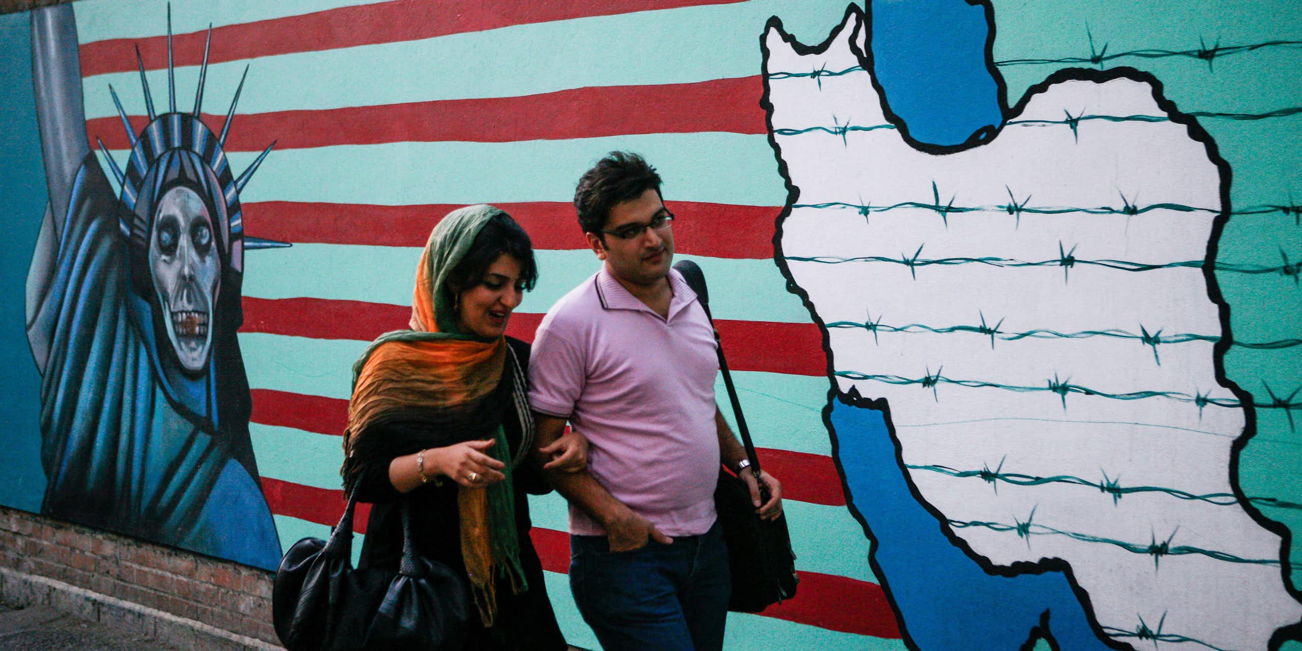 A man and woman walk past an anti-US mural on the walls of the former US embassy in Tehran.