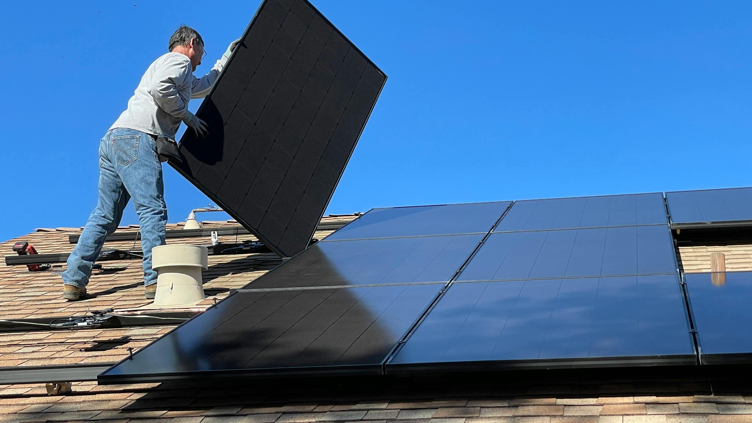 A man installs solar panels on a roof.
