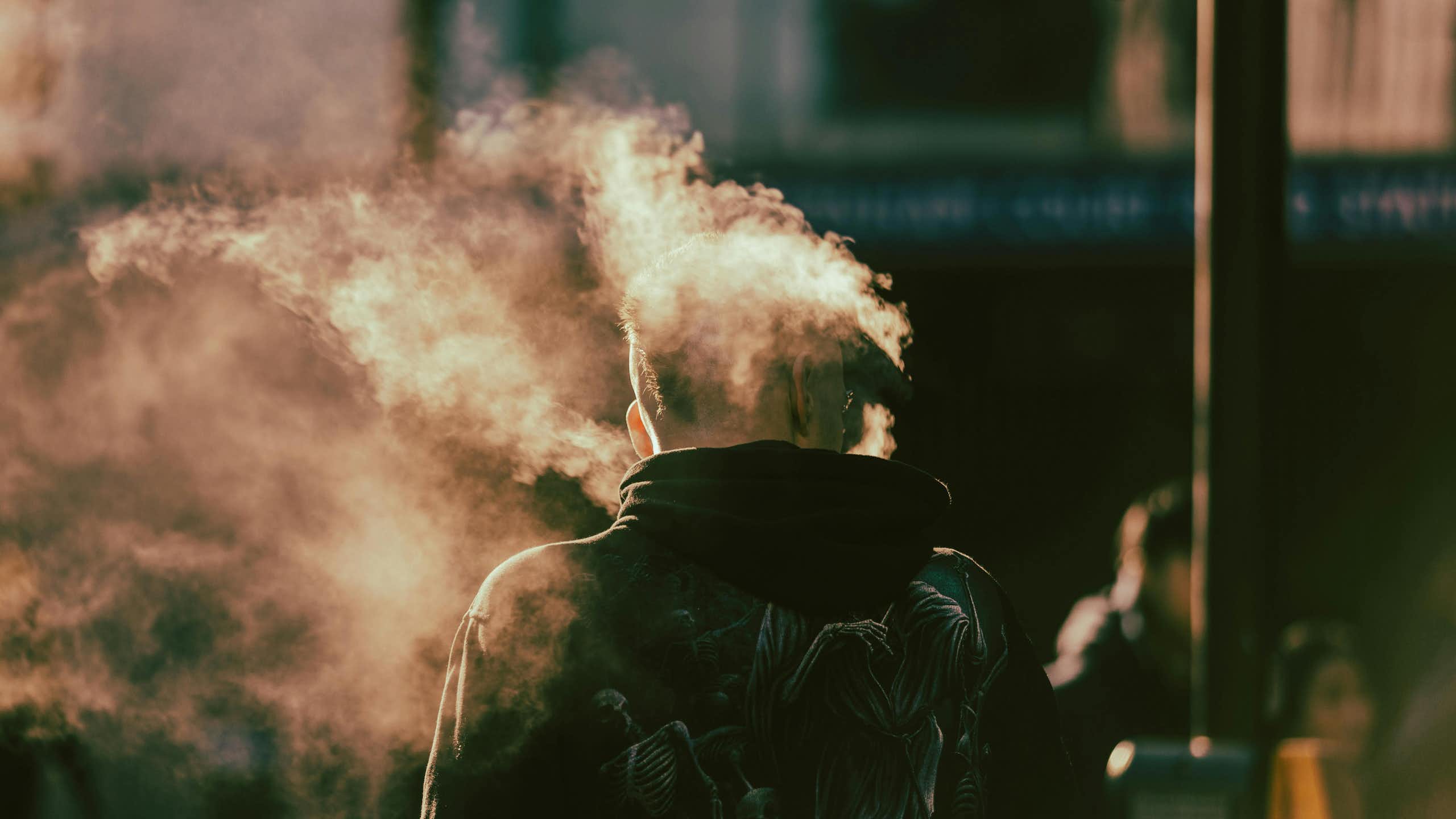 Back of a man vaping with mist around his head.