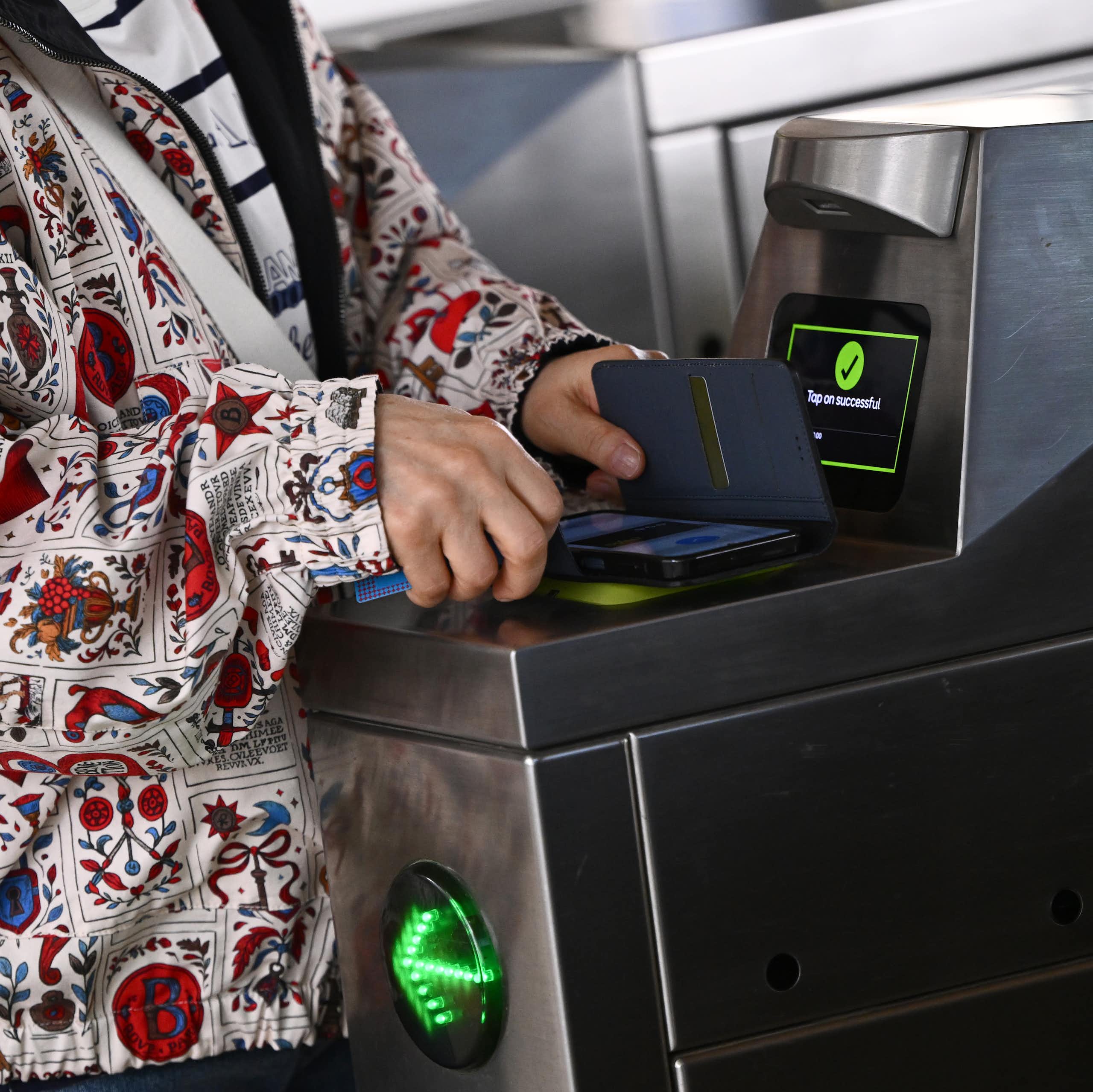A woman's hands holds a phone over a ticket scanner at a train station turnstile.