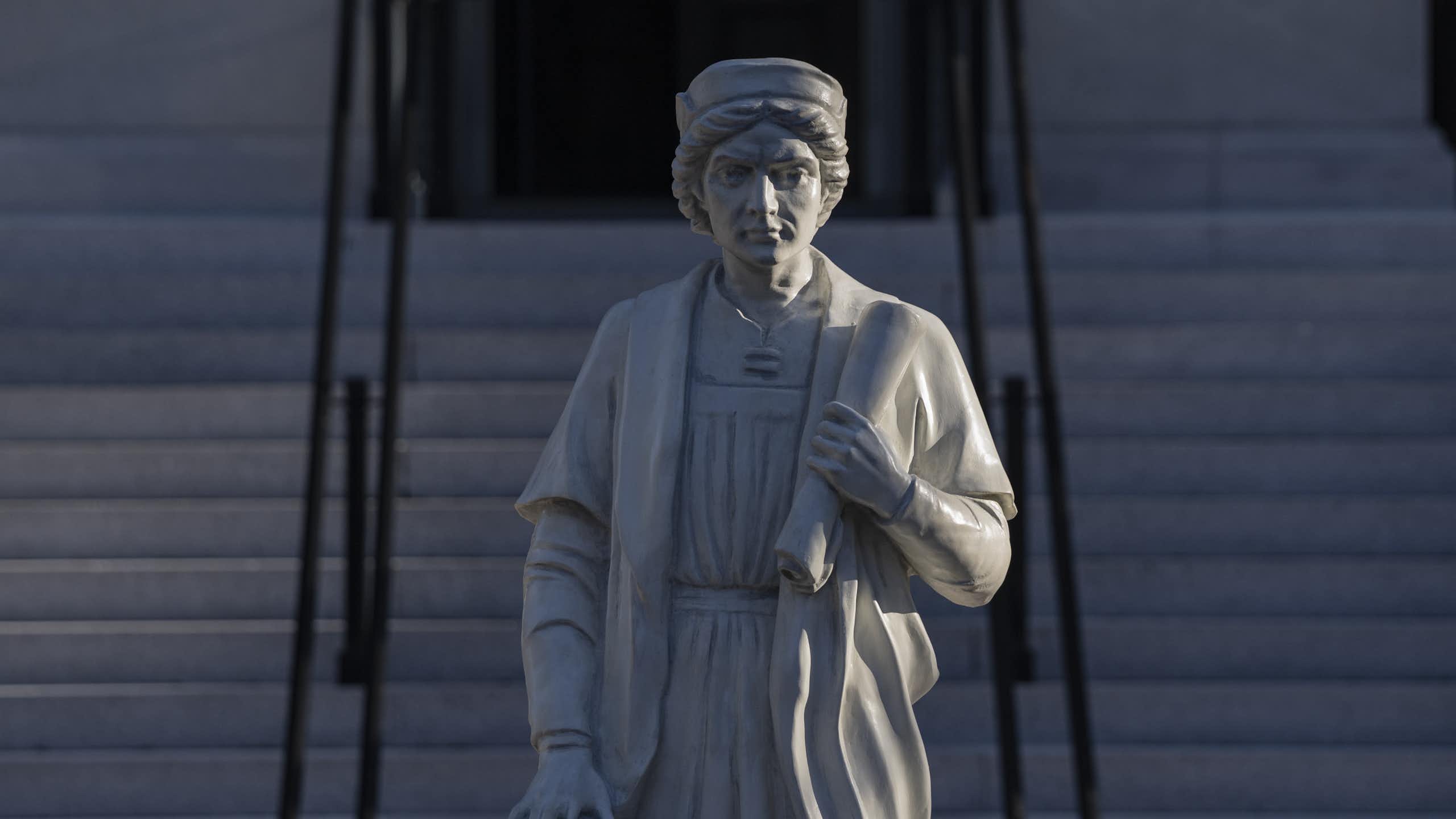 Statue of a man holding a scroll, with stairs in the background