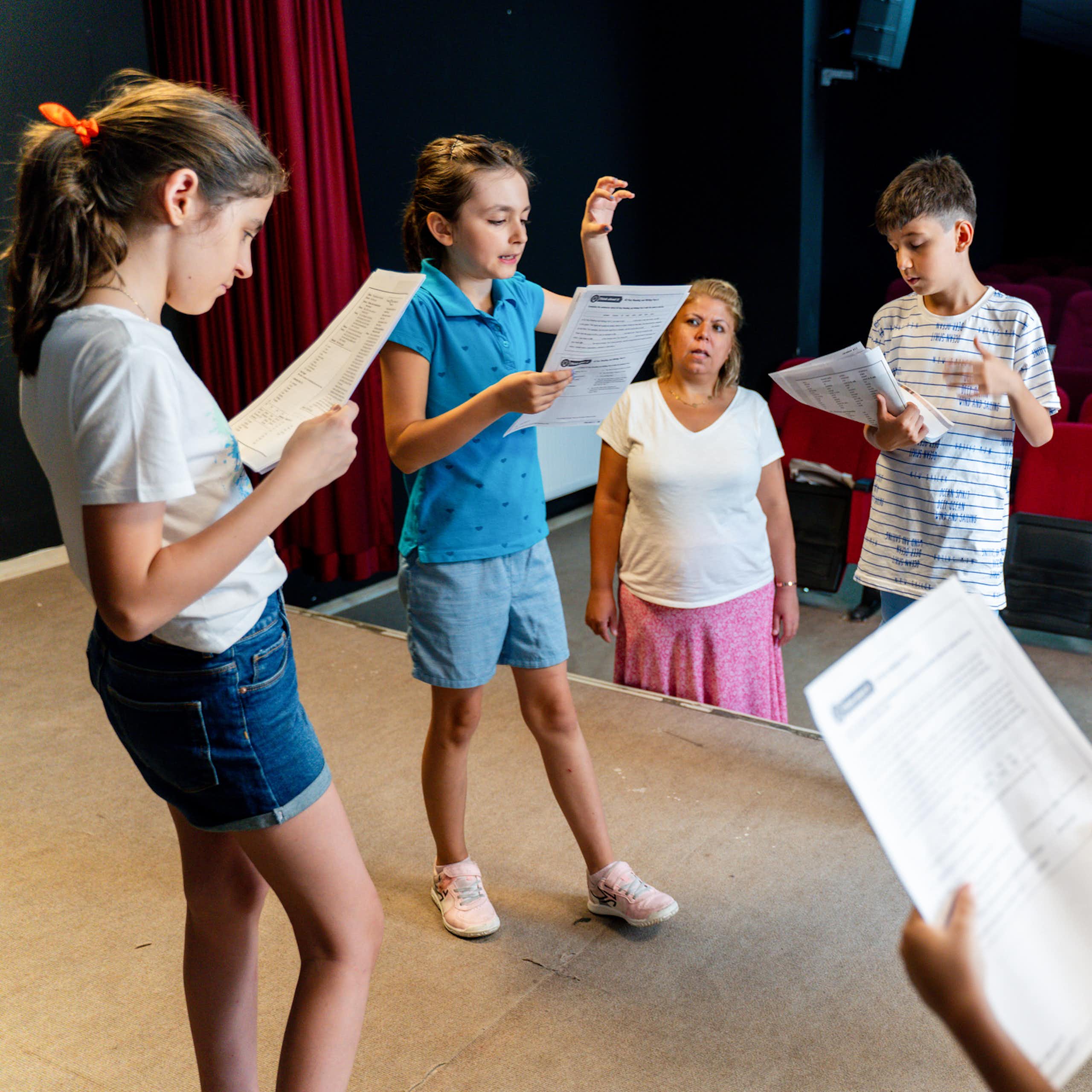 A group of children read scripts on a stage. 