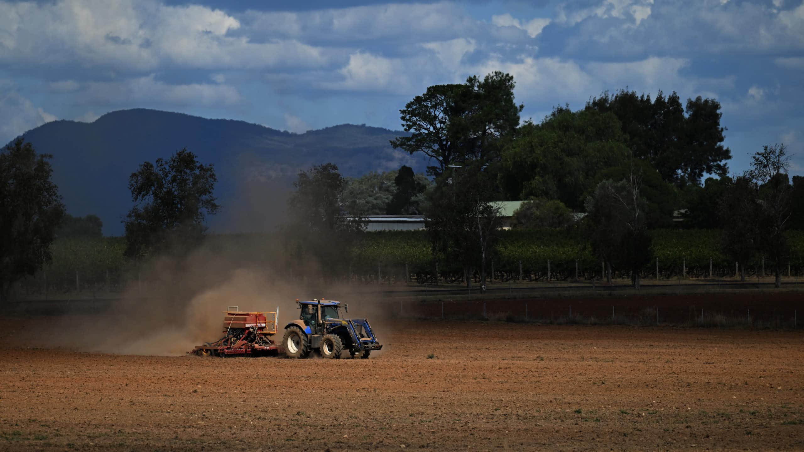 A tractor ploughs a dusty orange field. 