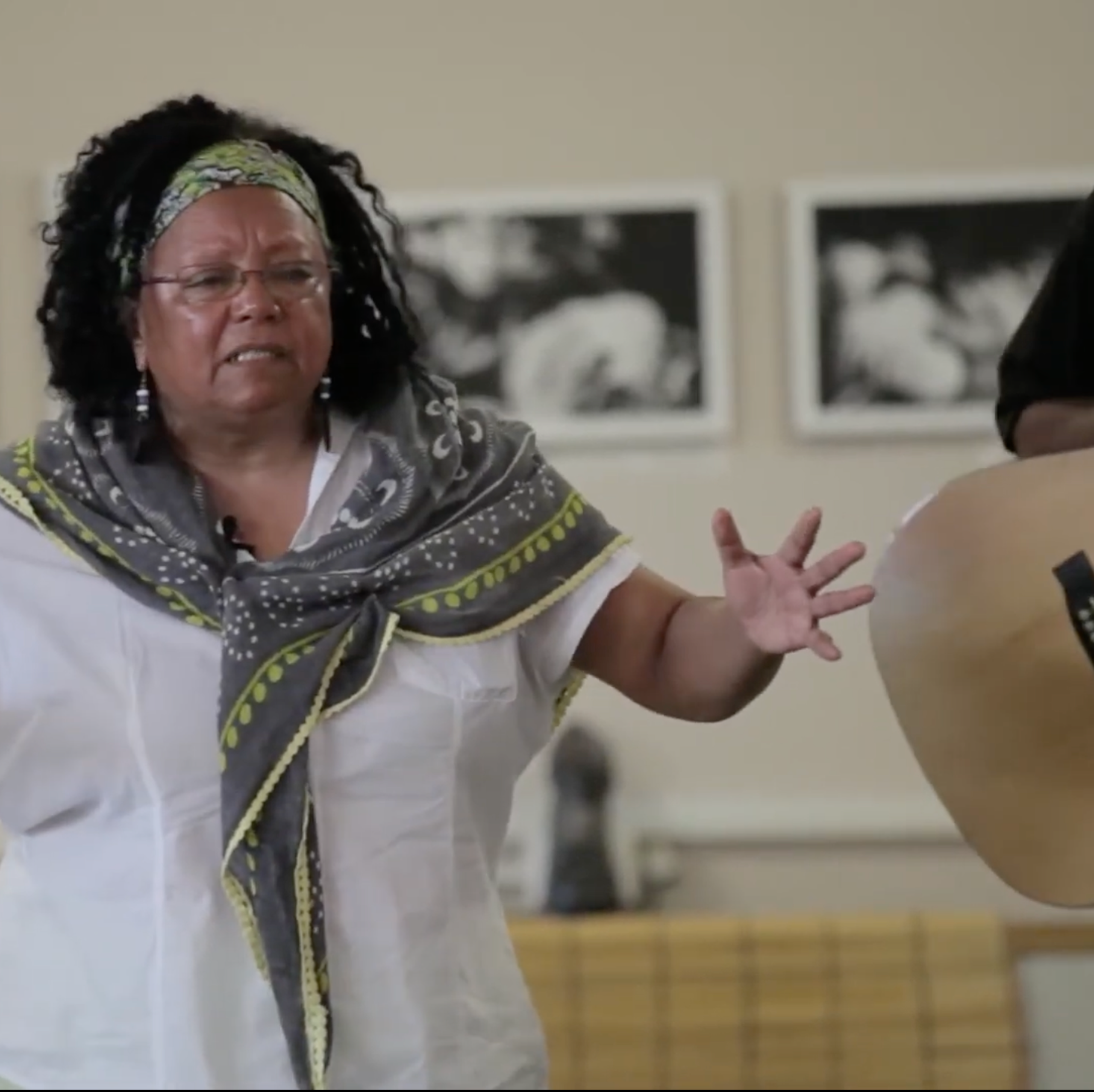 An African woman holds her arms apart in a gesture as she speaks alongside a man playing the guitar.